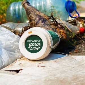 Garbage with "This Land is Your Land" printed on top of a discarded coffee cup